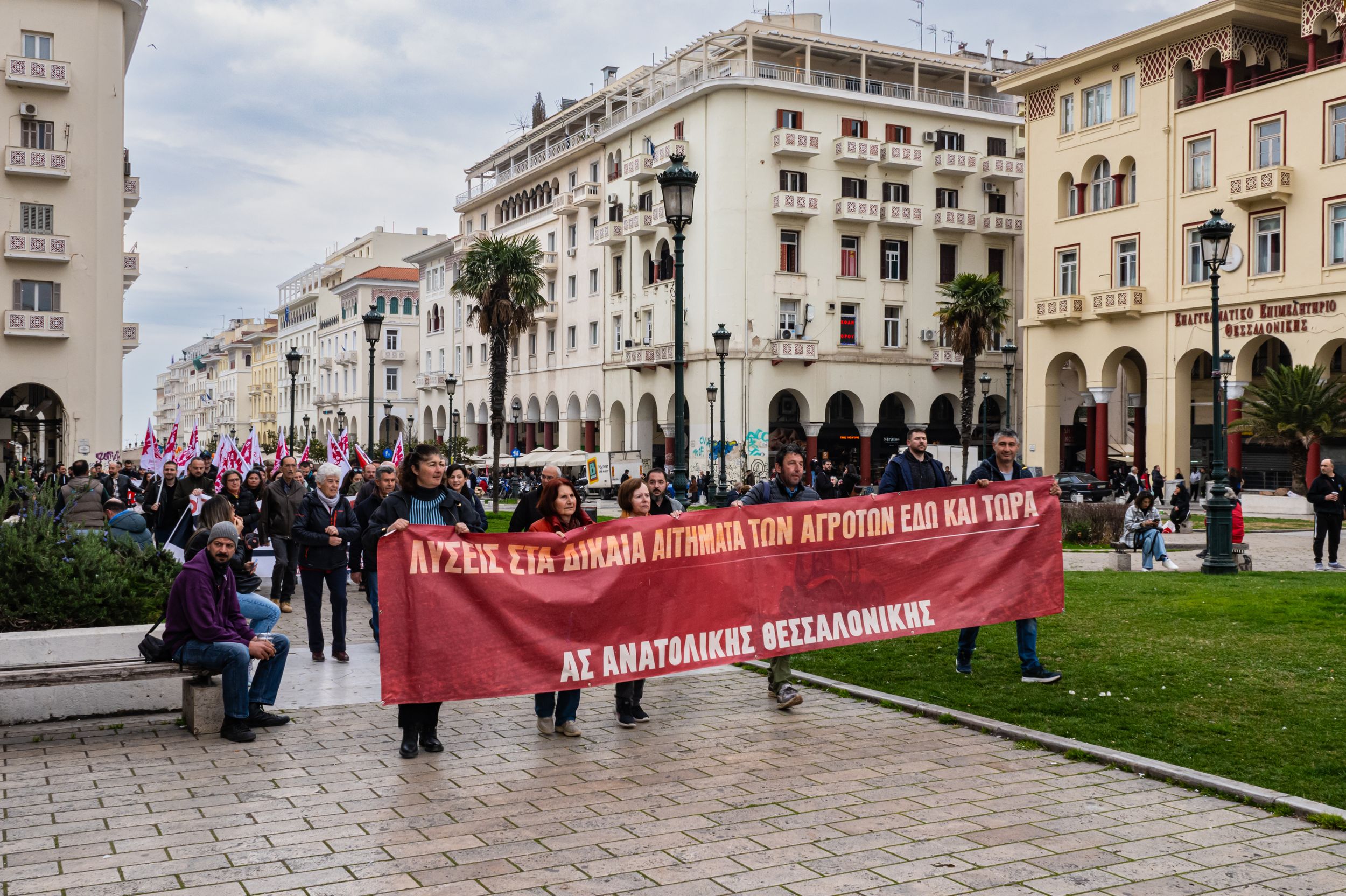 Protesters march in Thessaloniki city square holding a red banner during a Greek farmers demonstration.