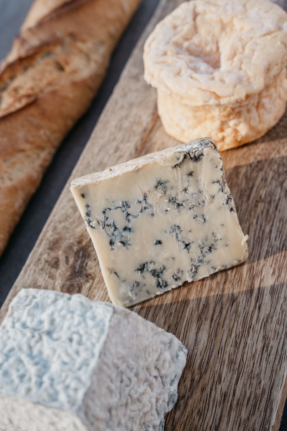 Assortiment de fromages, y compris le fromage bleu et les variétés de croûte molle exposées sur une planche de bois rustique avec du pain.
