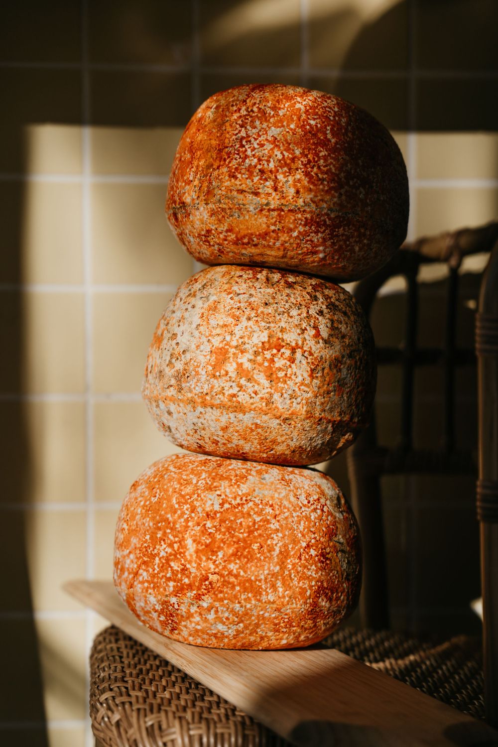 Trois pains ronds au levain empilés saupoudrés de farine sur une planche de bois au soleil chaud.