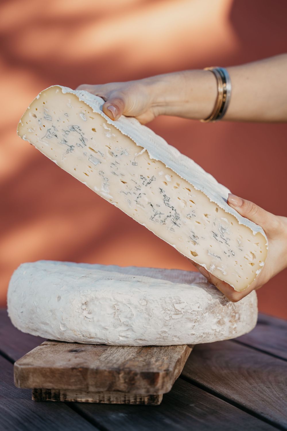 Mains tenant une tranche de fromage bleu avec de la croûte blanche sur une roue entière sur une planche de bois.