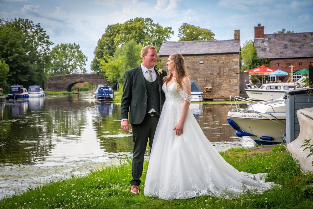 Bride and groom share a romantic moment by a scenic canal with boats in the background.