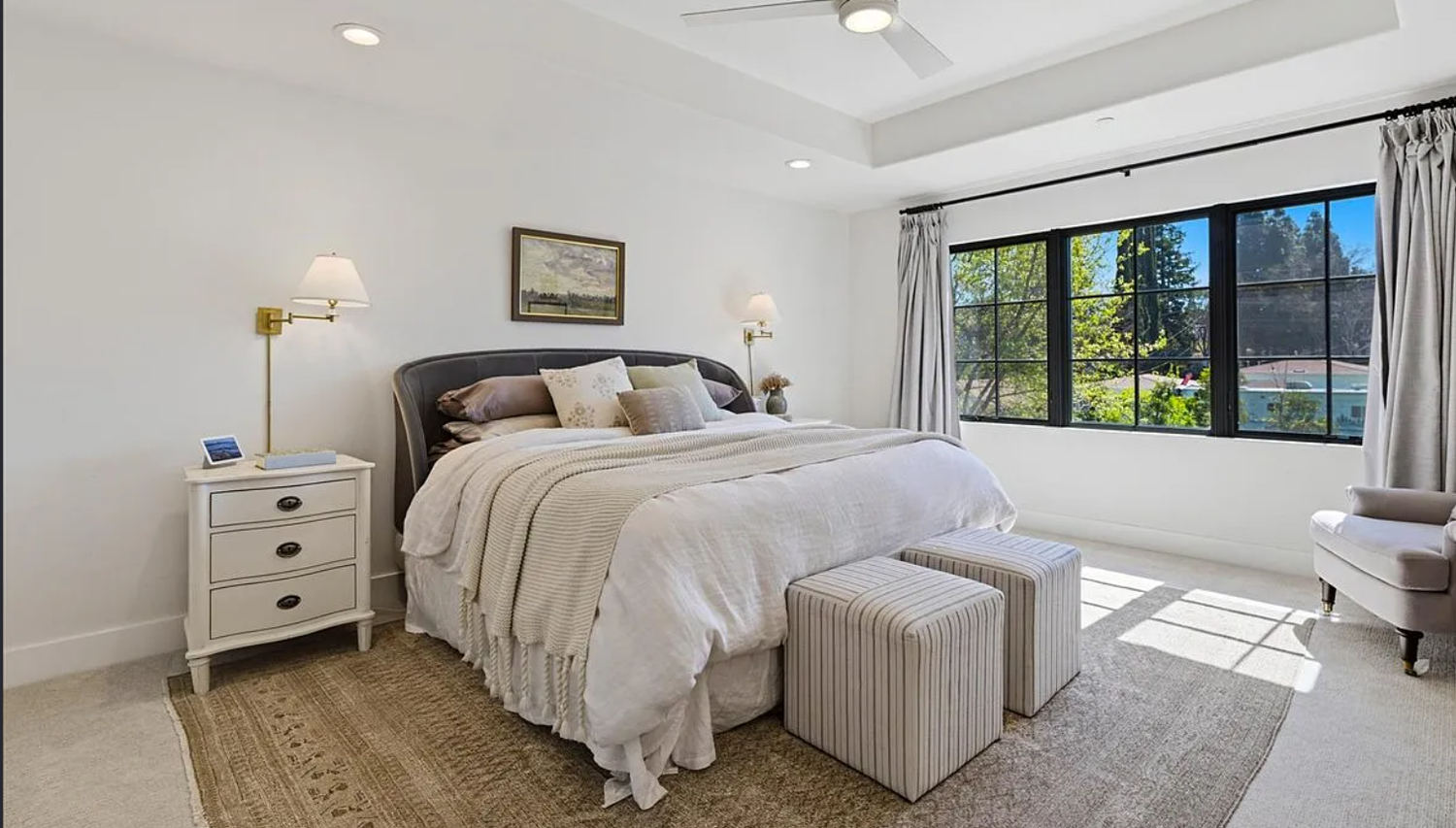 Modern bedroom interior with white bedding, natural light from windows, and minimalist decor in a coastal style.
