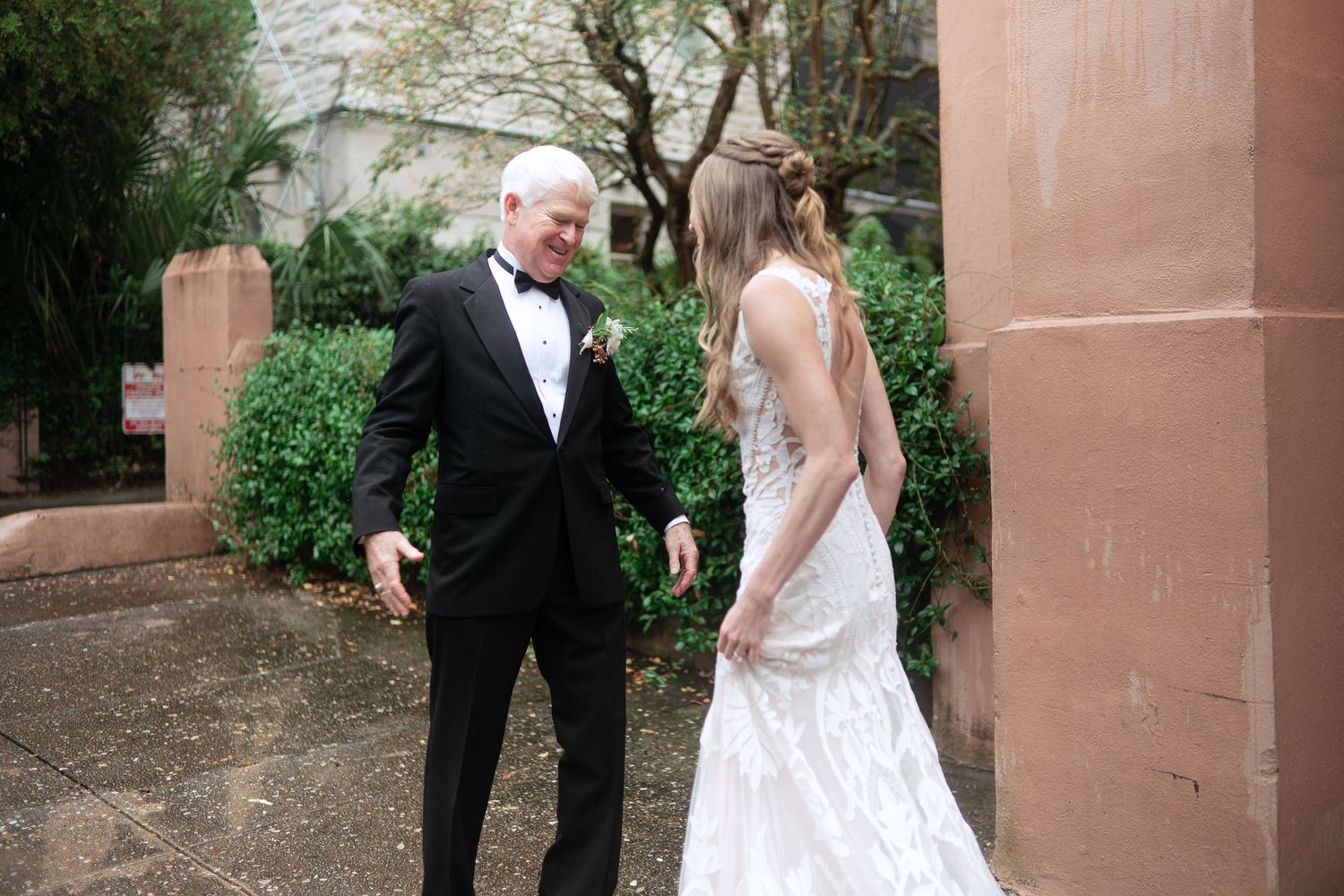 Wedding portraits taken against a pink stucco building in a garden setting.