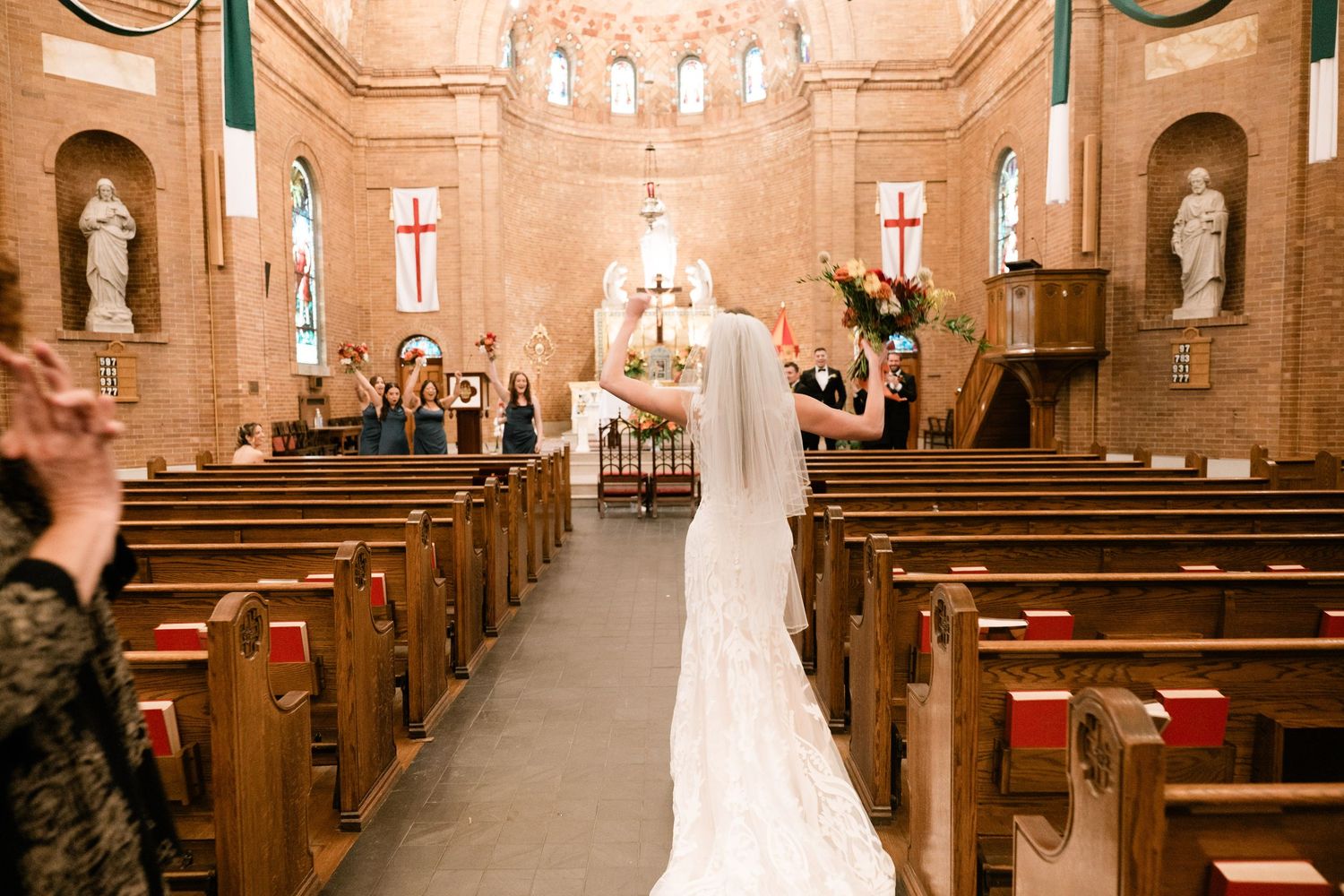 A long white wedding dress train trails down the center aisle of a traditional church with wooden pews.