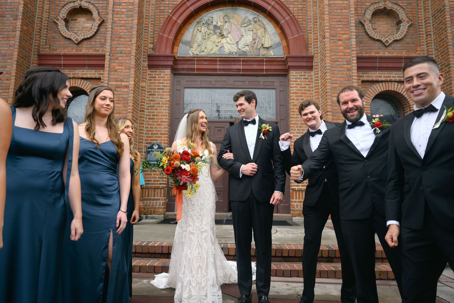 Wedding party lined up outside historic brick church with ornate architecture.