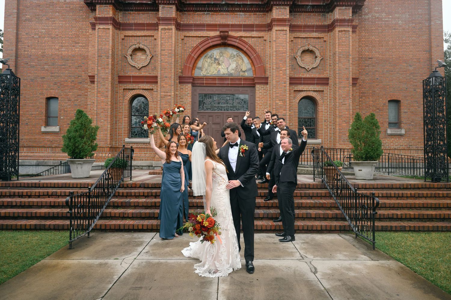 Wedding celebration outside red brick church with ornate architectural details.