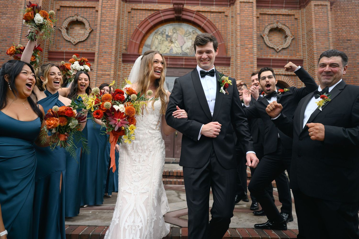 Wedding party in navy and black attire posing in front of brick church exterior.