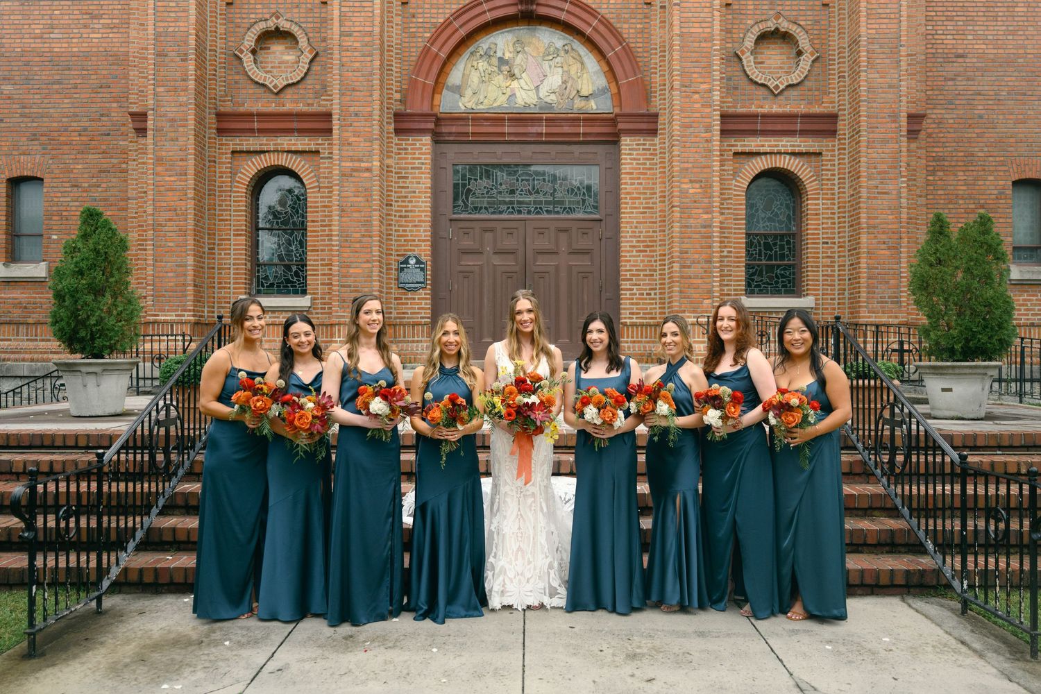Wedding party in teal blue dresses poses together outside a brick church building.