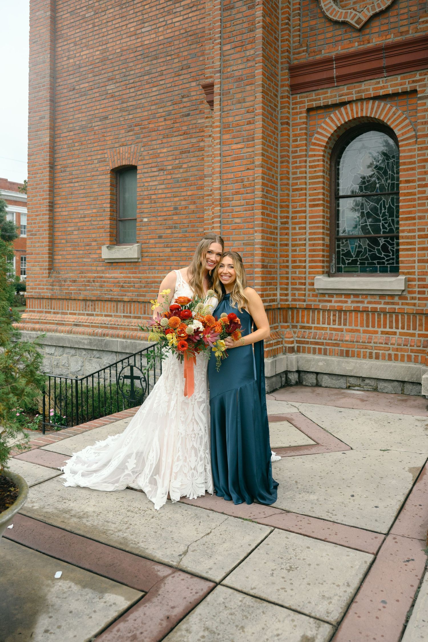 Wedding party members in teal and white pose outside historic brick church entrance.