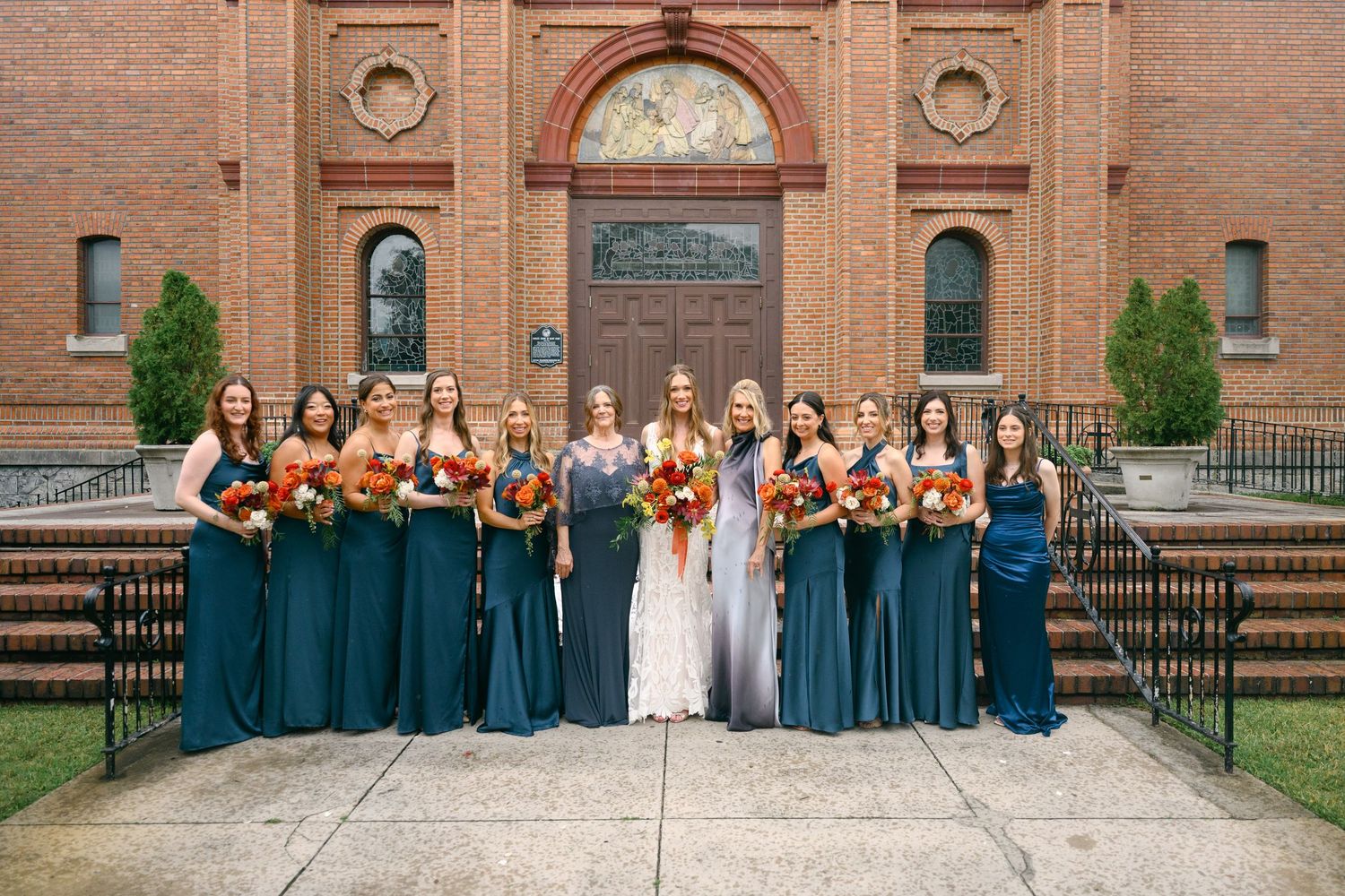 Large wedding party stands arranged on church steps with bridesmaids in teal gowns and groomsmen in dark suits.