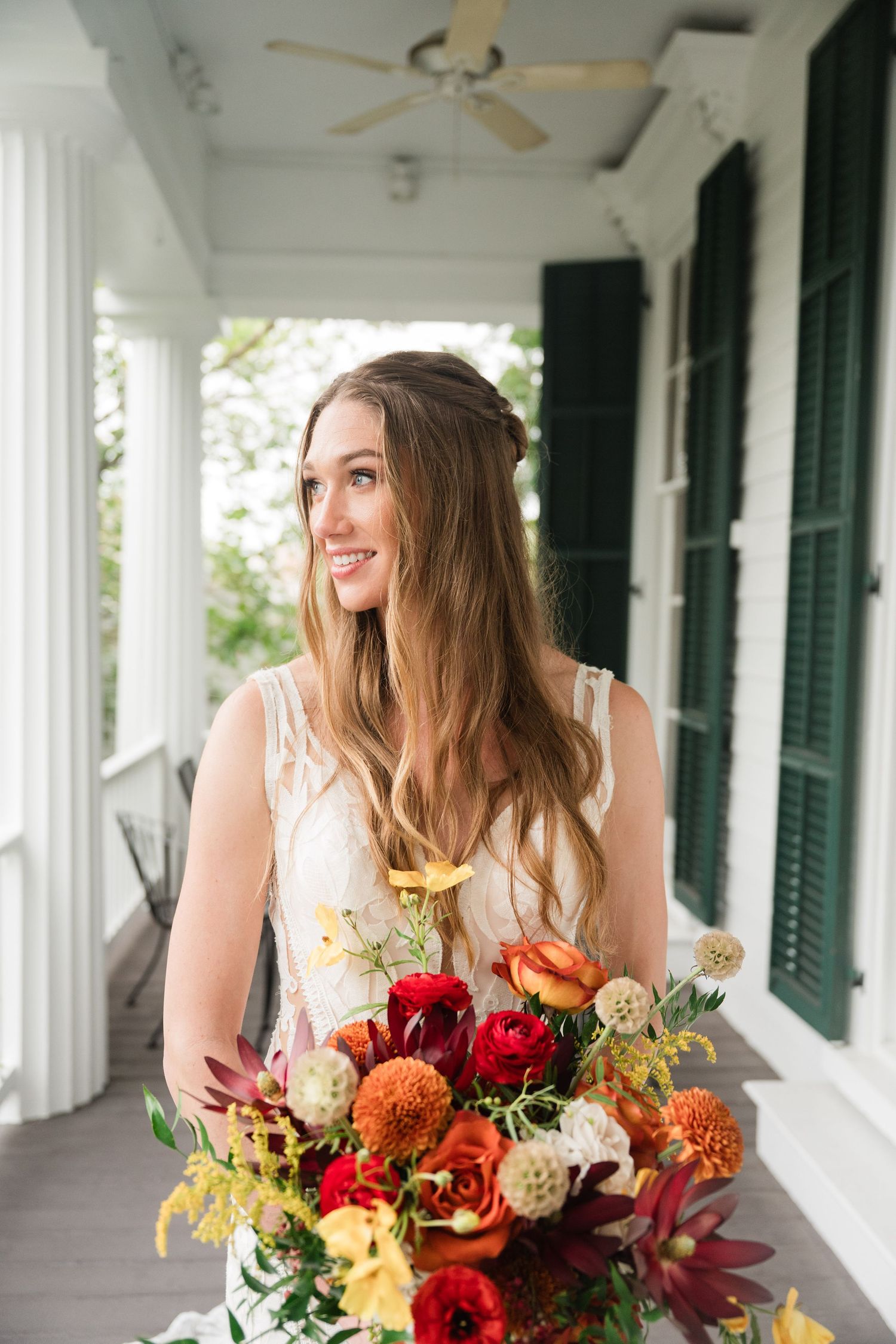 Beautiful fall wedding bouquet with red and orange flowers displayed on a white porch with columns.
