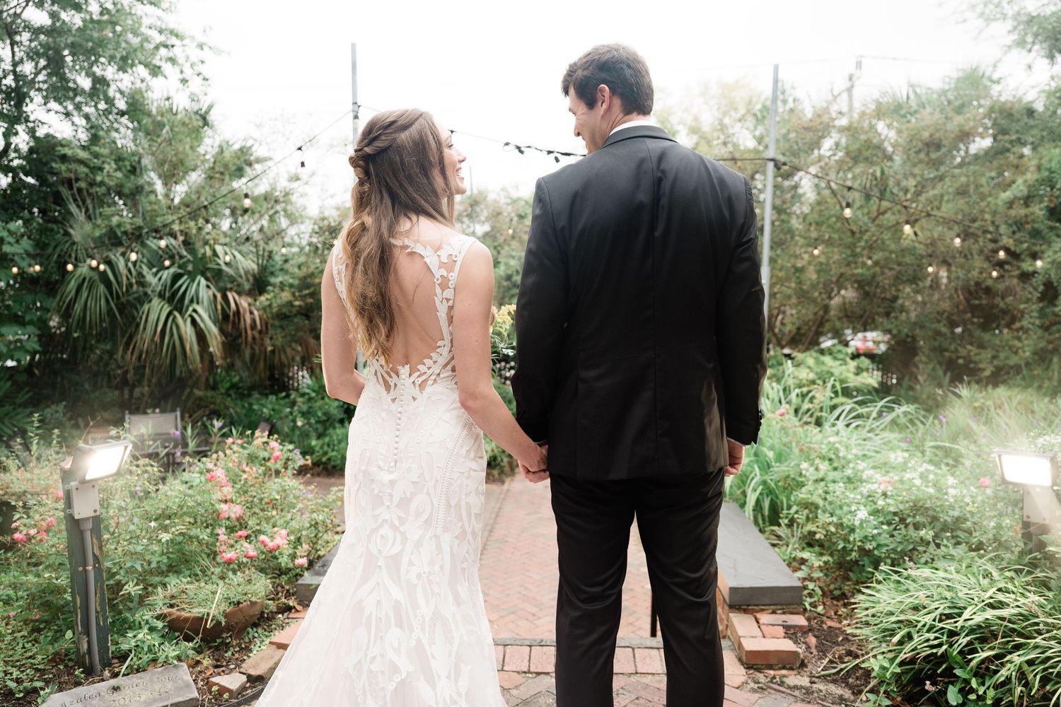 Couple walking together through lush garden pathway in wedding attire.