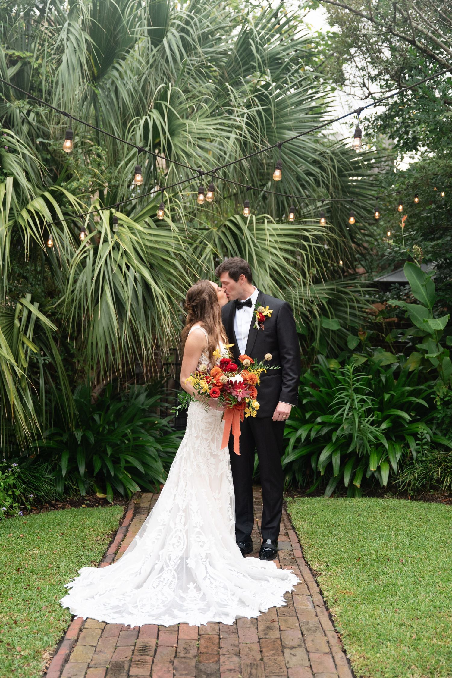 Romantic wedding couple shares intimate moments on a brick path surrounded by lush tropical palm gardens.