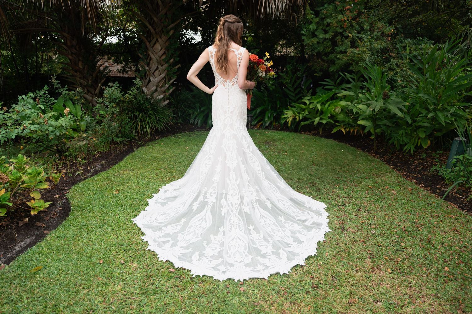 Wedding dress train elegantly spread out on green grass in an outdoor garden setting.