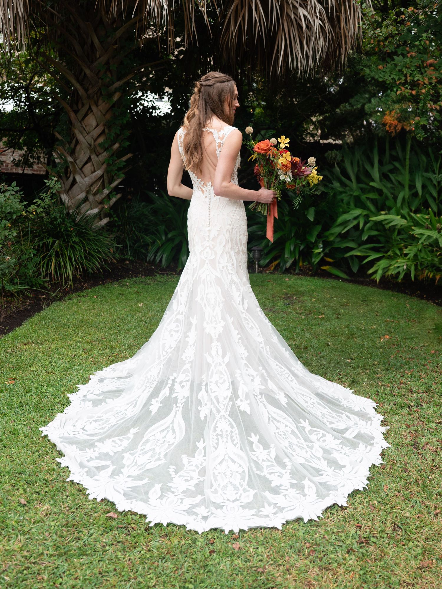 Stunning lace wedding dress with dramatic cathedral train displayed on green lawn surrounded by tropical foliage.