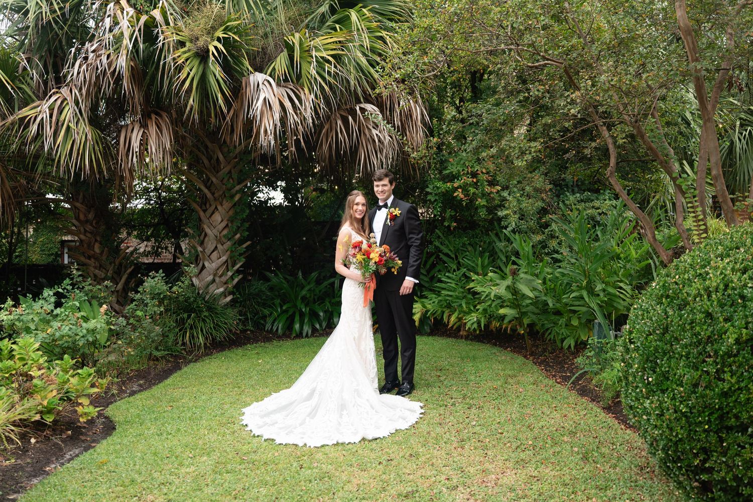 Wedding couple poses along a winding brick pathway in a tropical garden setting with palm trees.