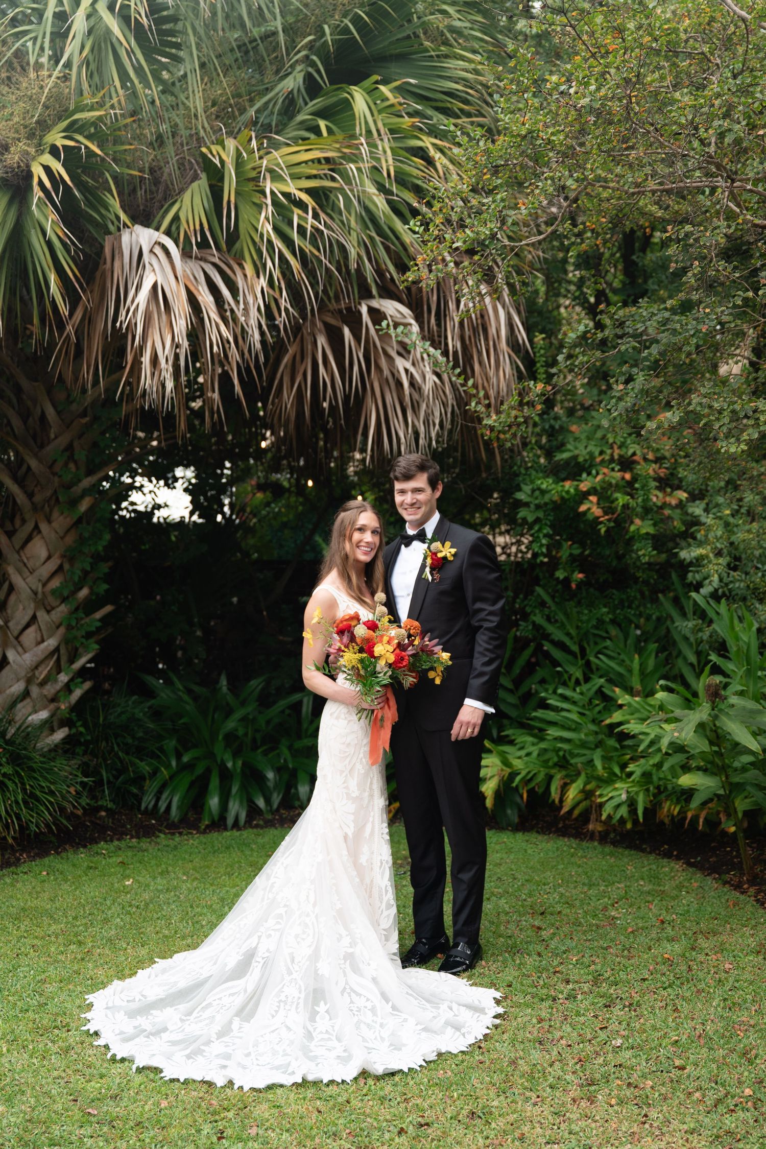 A couple poses in a lush tropical garden setting with palm trees and greenery for their wedding portraits.
