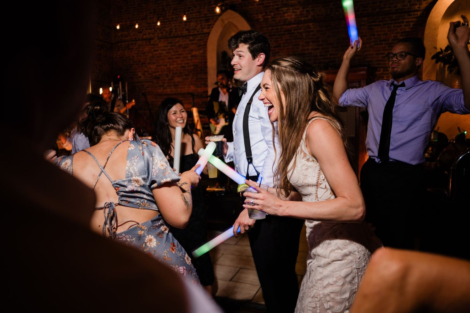 Wedding reception guests dancing and celebrating on a dimly lit dance floor with colorful lighting effects.