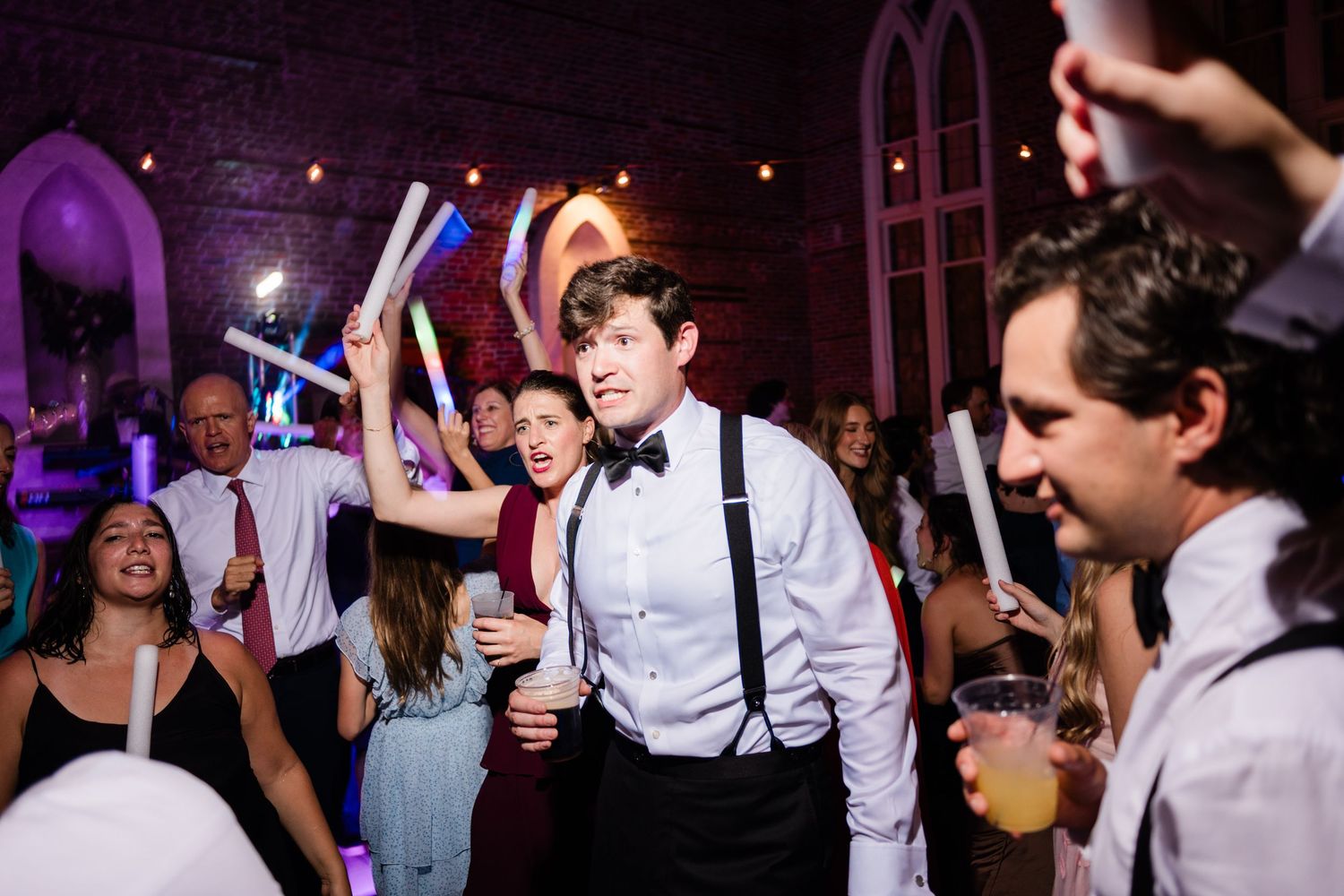 Lively dance party scene with guests holding glow sticks under purple ambient lighting.