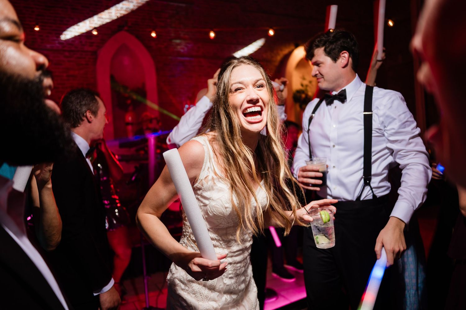 Wedding reception dance party with colorful red lighting and couples dancing on the dance floor.
