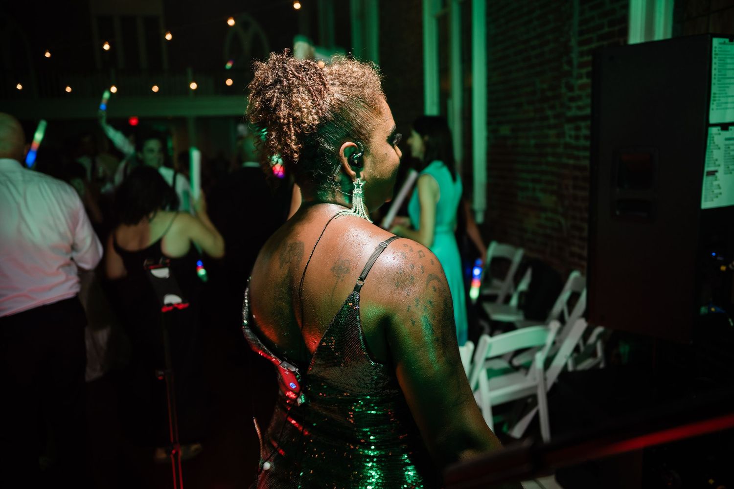 A person in a sparkly dress dances at a dimly lit venue with green lighting and string lights overhead.