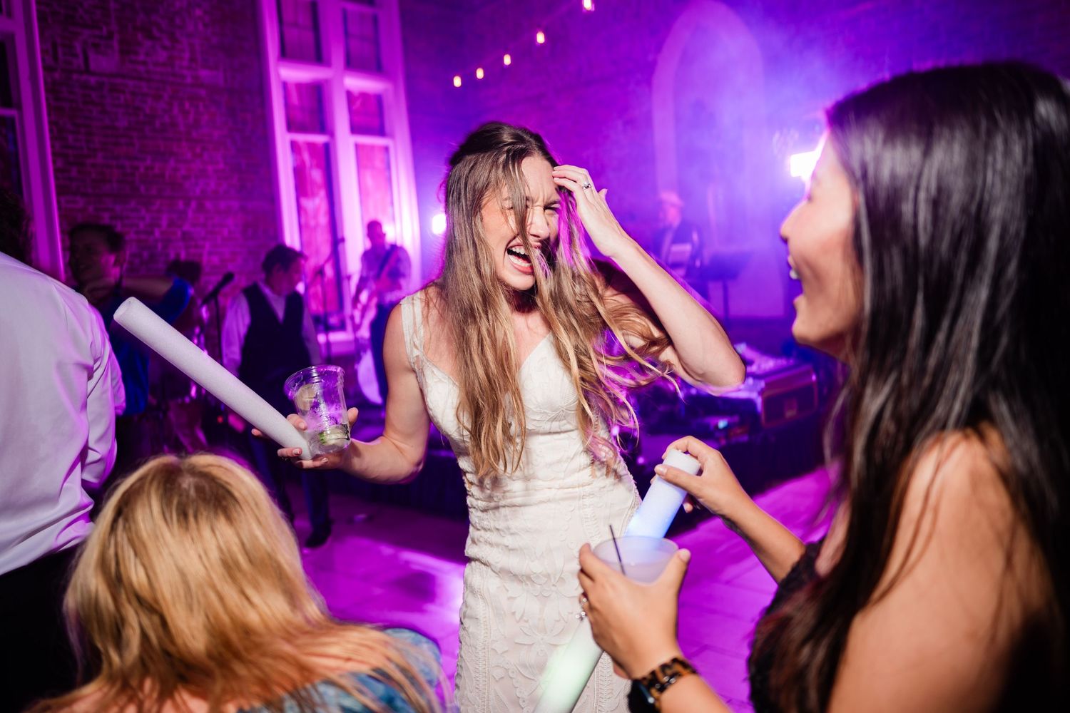 Wedding celebration with purple uplighting and guests dancing with glow sticks on the dance floor.