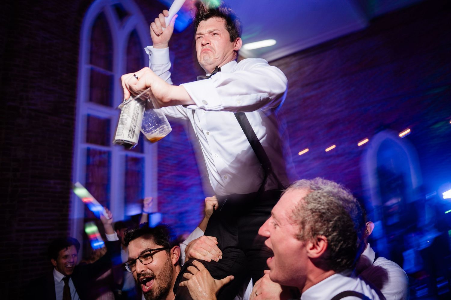 People celebrating at a formal event with blue lighting and raised drinks in a festive atmosphere.