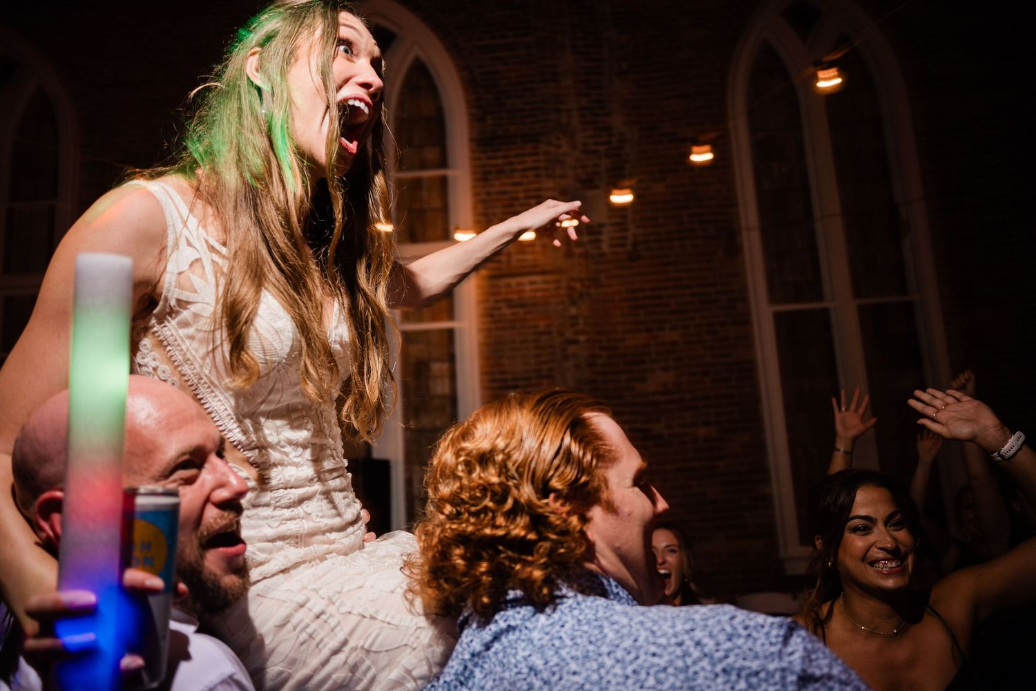Wedding celebration in full swing with guests dancing under warm lighting in a rustic brick venue.