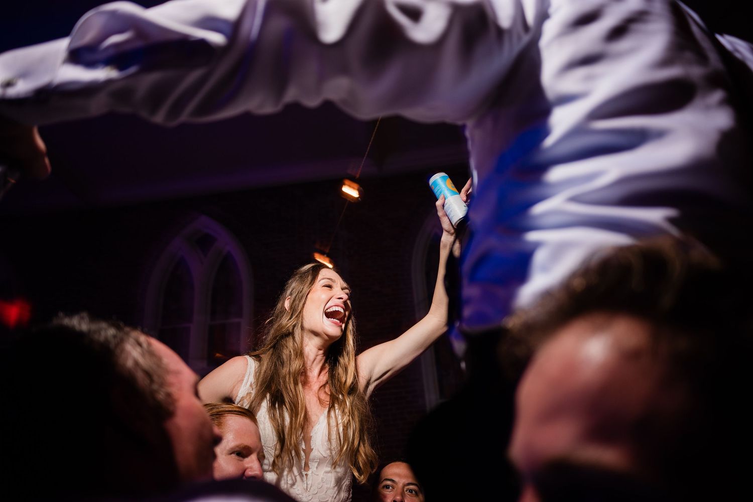 Concert crowd dances with raised arms at a nightclub with colorful lighting and atmospheric effects.