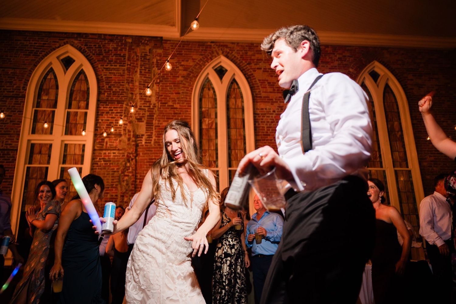 Wedding guests enjoying themselves on the dance floor in a rustic venue with arched windows.