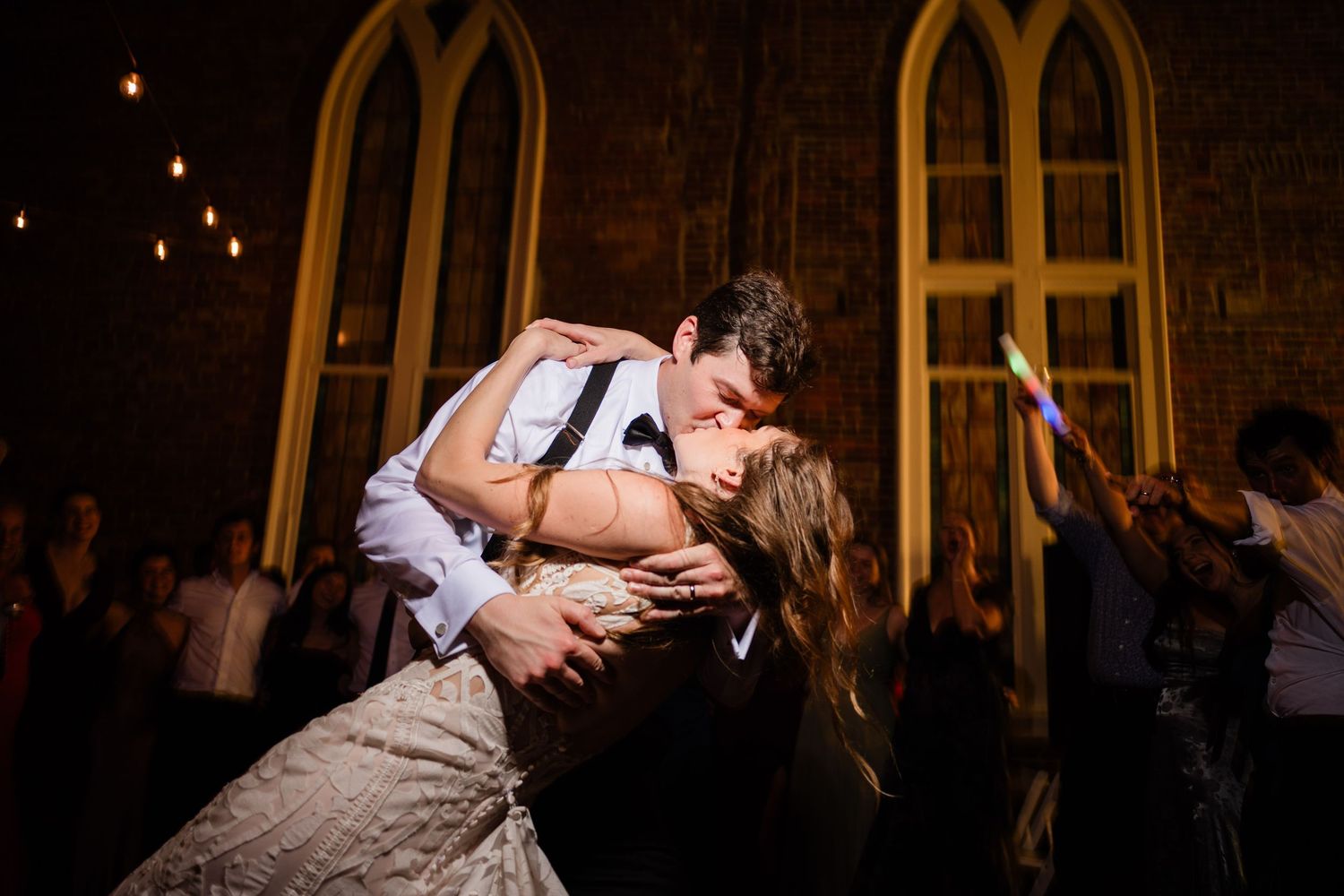 A couple shares a romantic dip during their first dance at a wedding reception in a dimly lit venue.