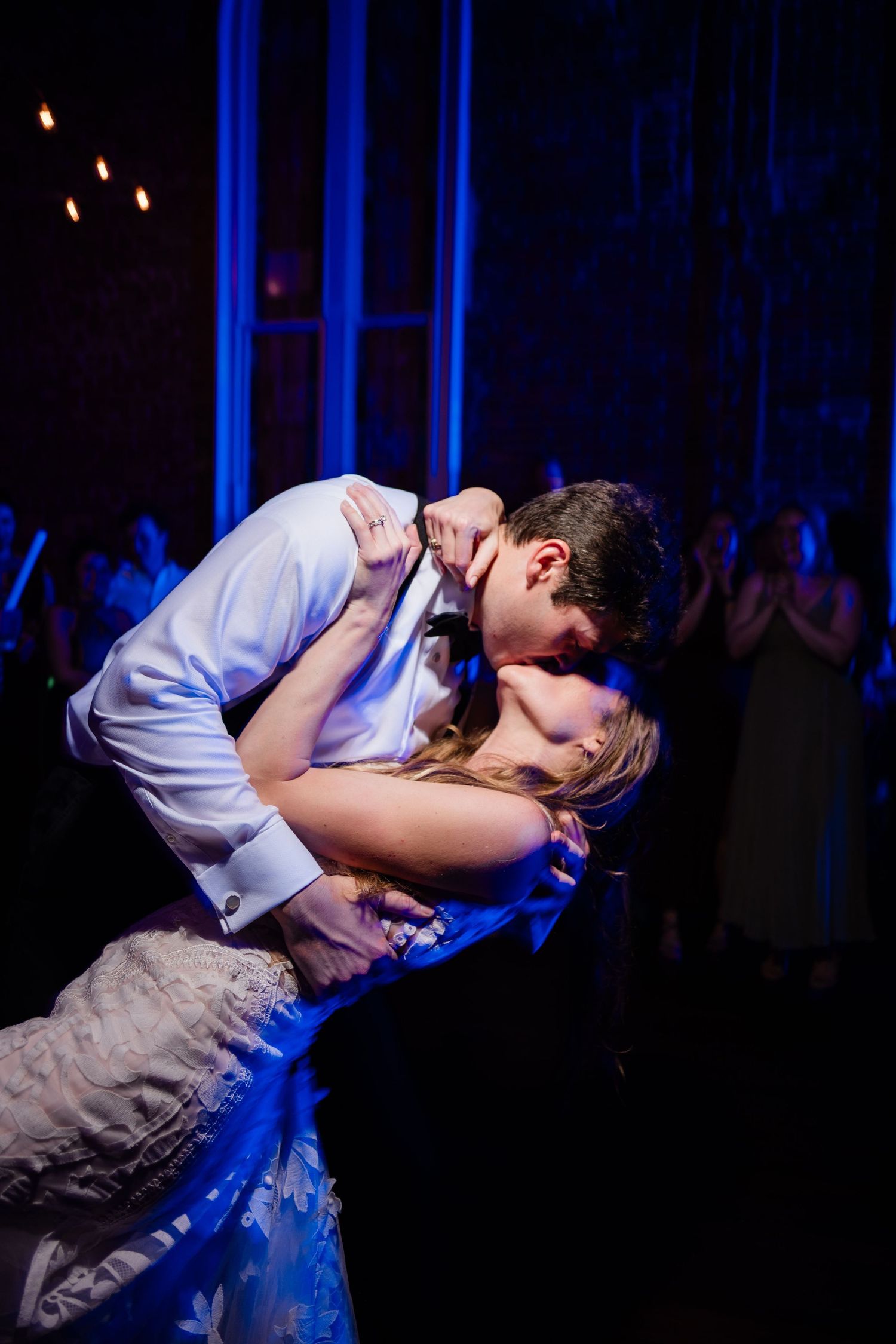 A romantic dance dip captured in dramatic blue lighting during a wedding reception.
