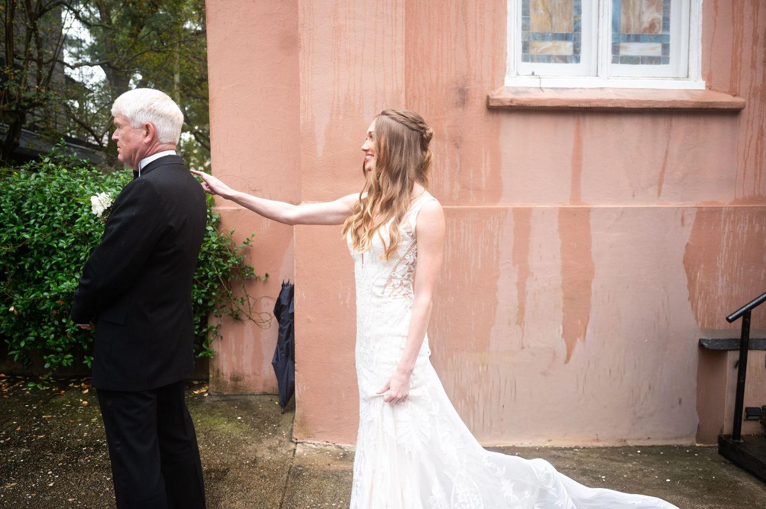 Wedding couple walking along a pink stucco building exterior.