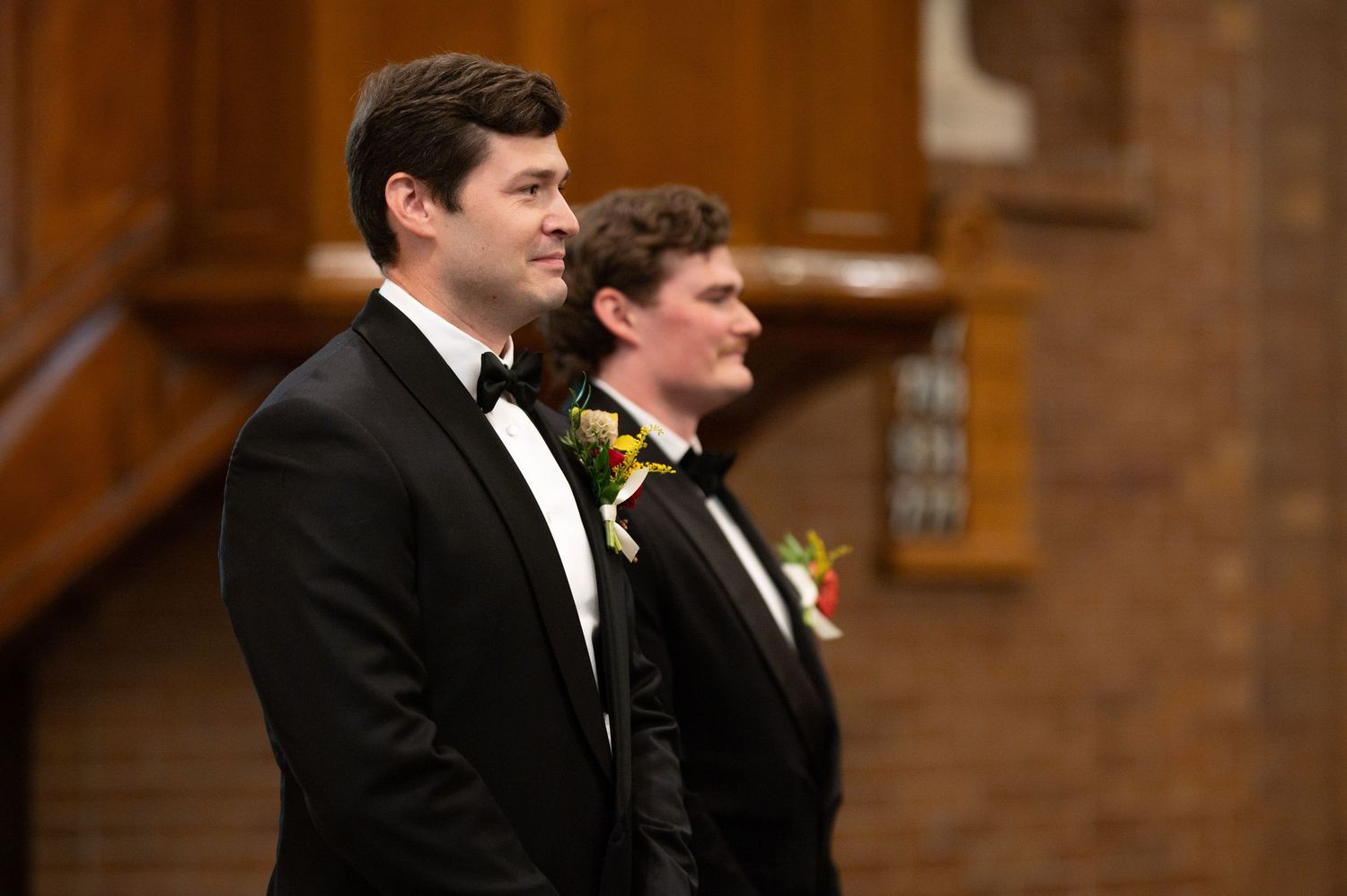 Groomsmen in black tuxedos standing together during wedding ceremony.