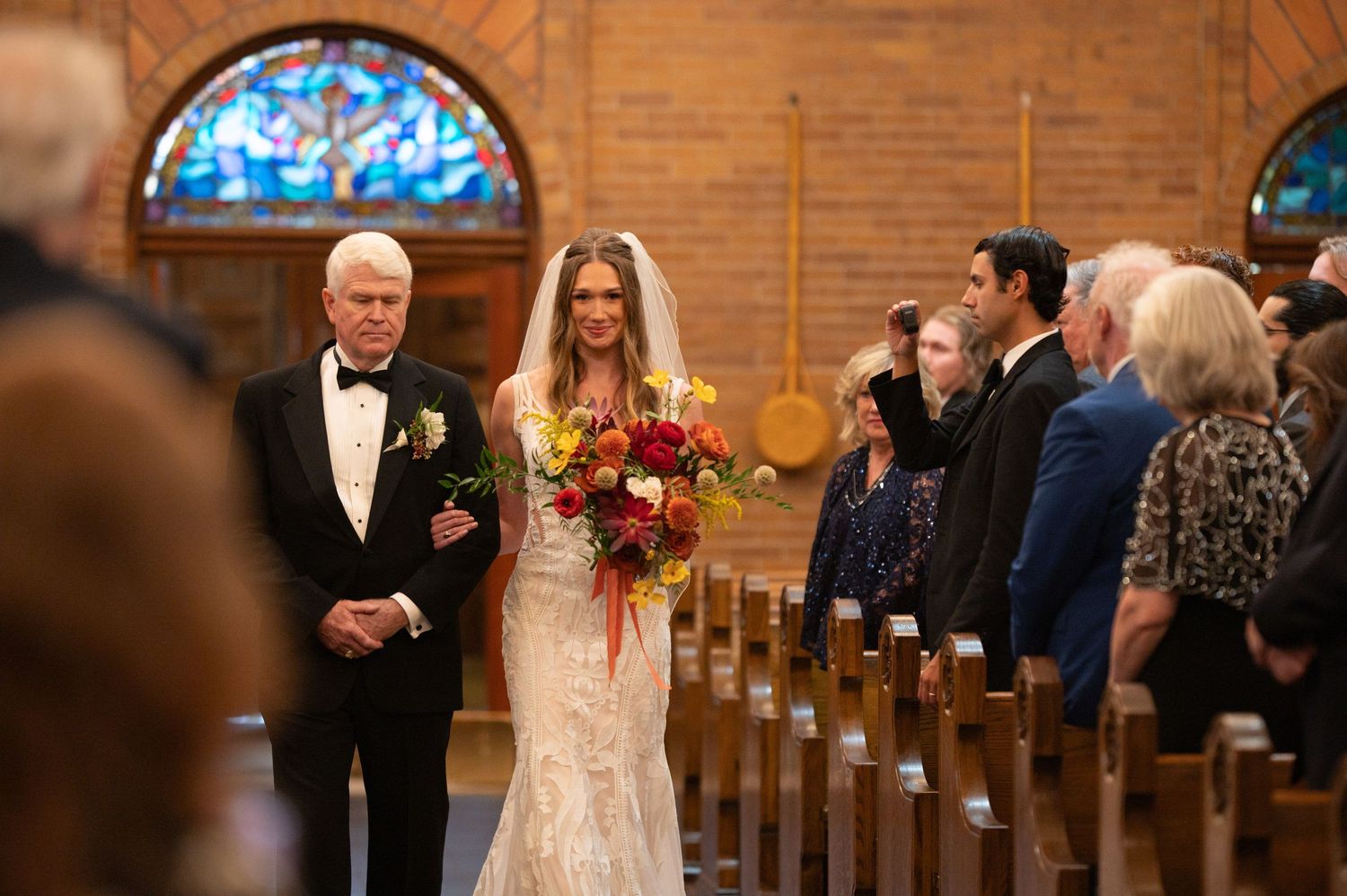Traditional church wedding ceremony with wooden pews and stained glass windows in warm lighting.