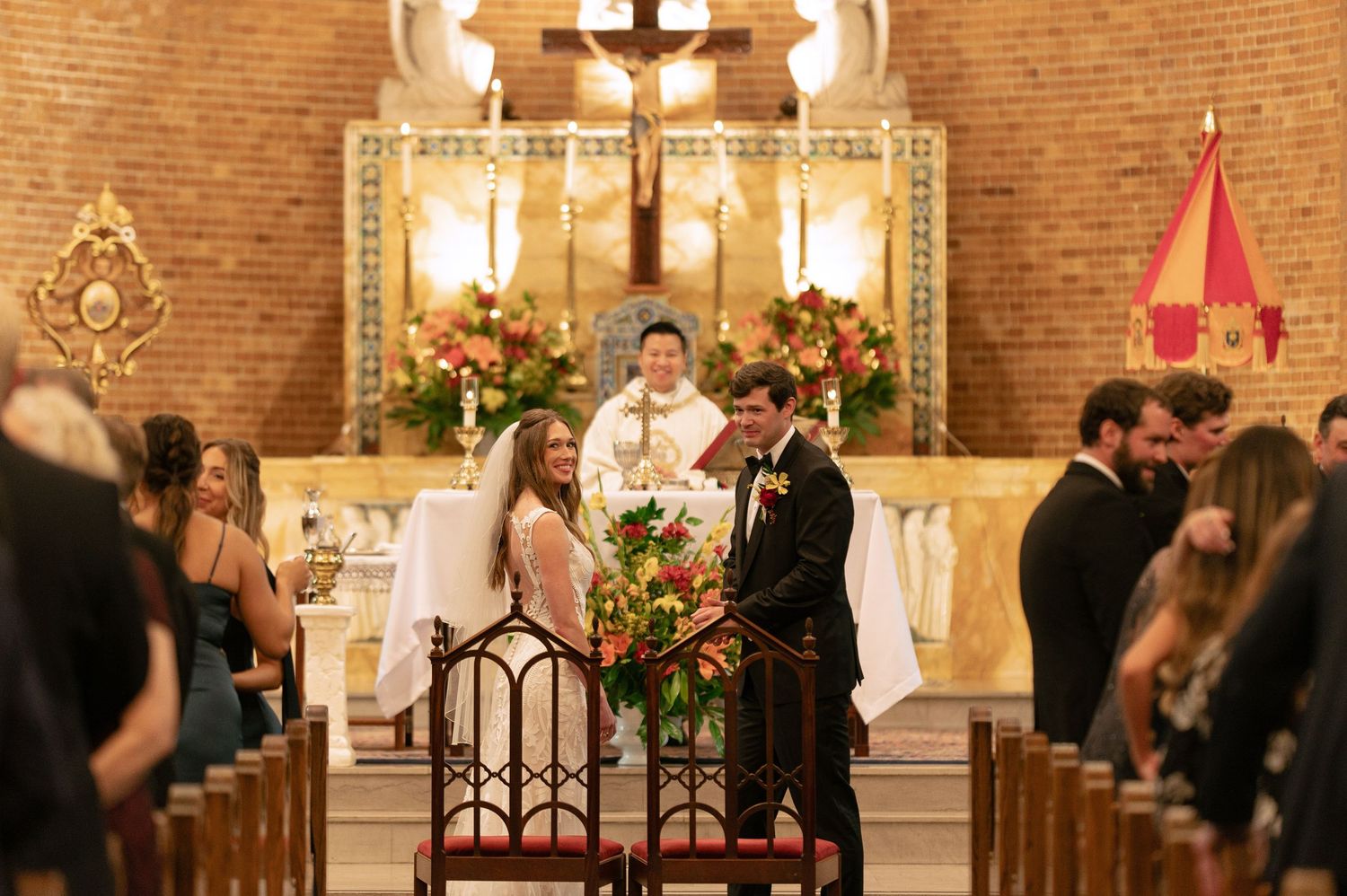 Wide view of wedding ceremony in progress inside beautiful brick church with decorative altar.