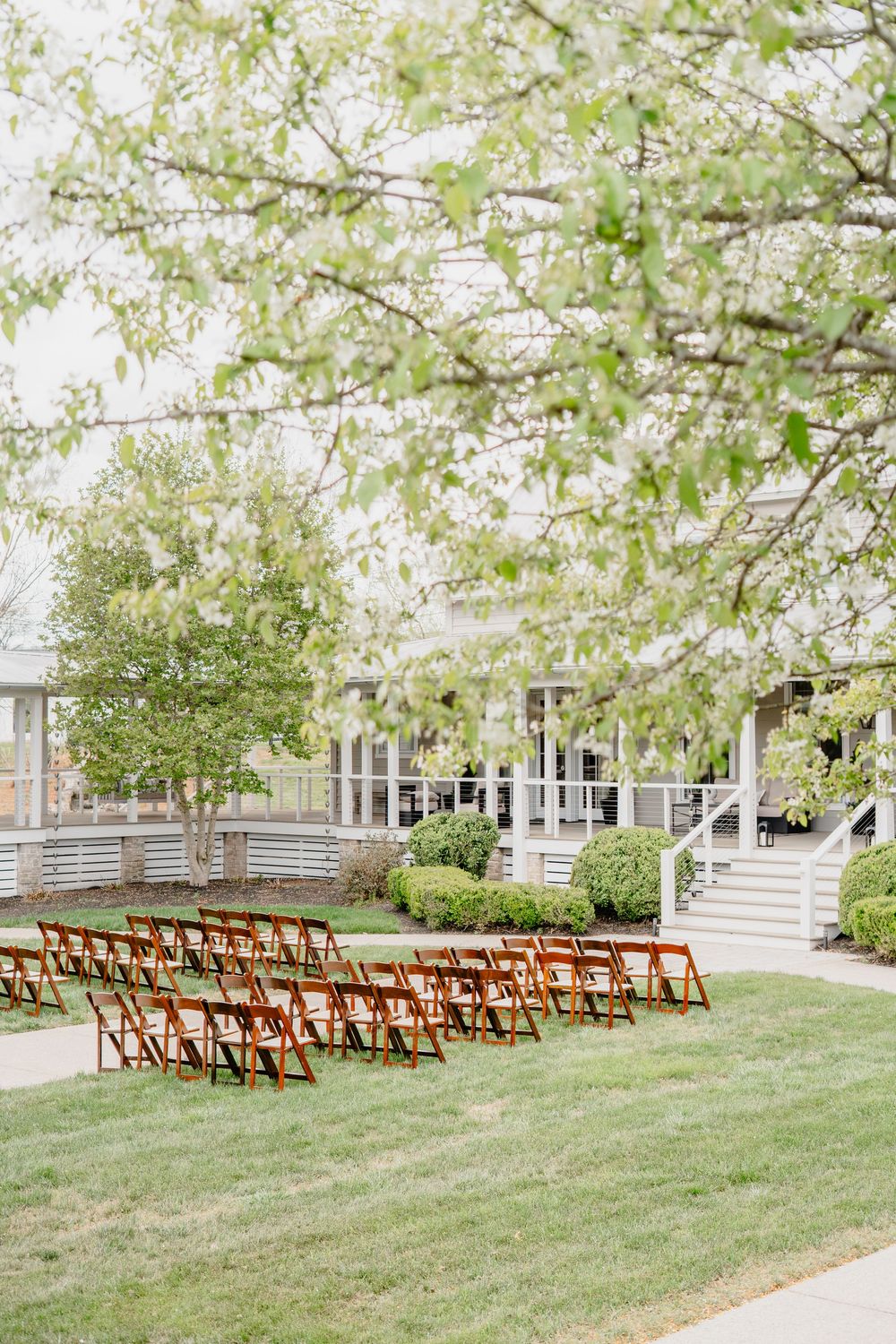 Rows of wooden folding chairs set on green lawn for outdoor wedding ceremony beneath blooming spring trees.