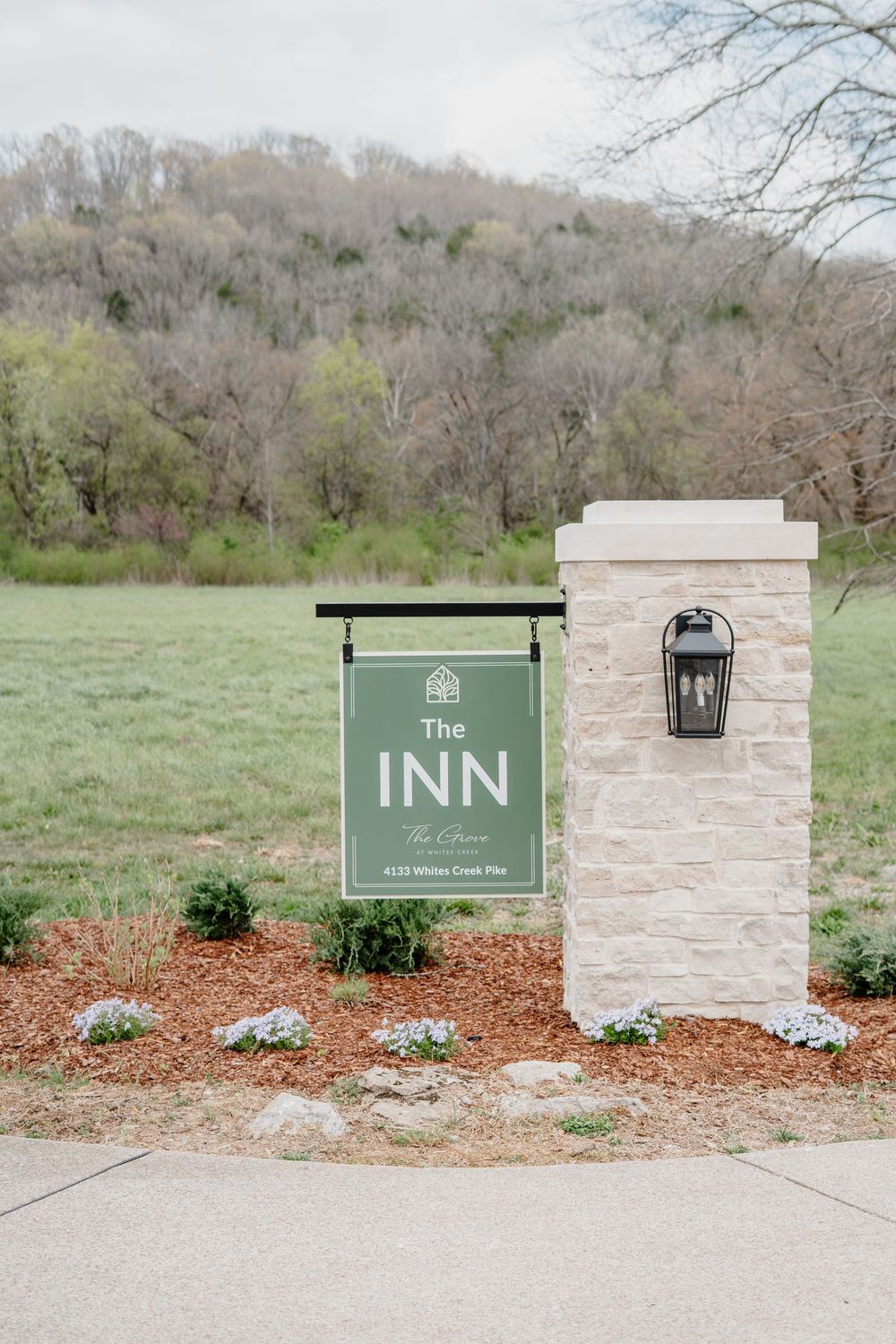 Entrance sign for The Inn at The Columns on stone pillar with lantern, surrounded by landscaping and wooded hills.