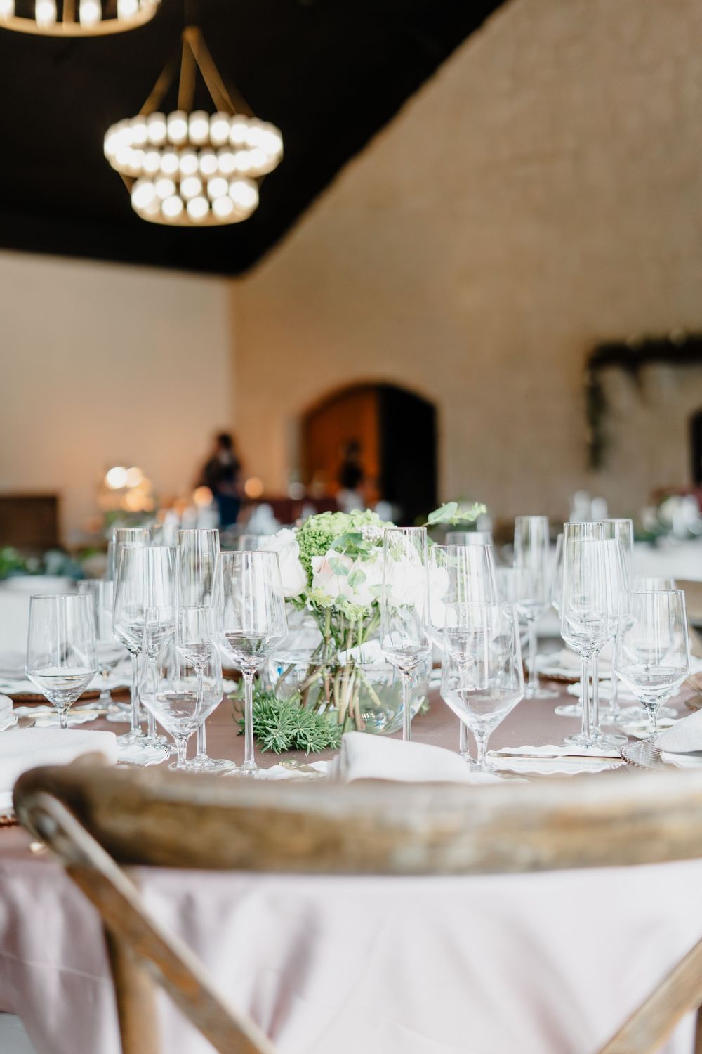 Elegant wedding reception table set with crystal glassware and white floral centerpiece under a chandelier.