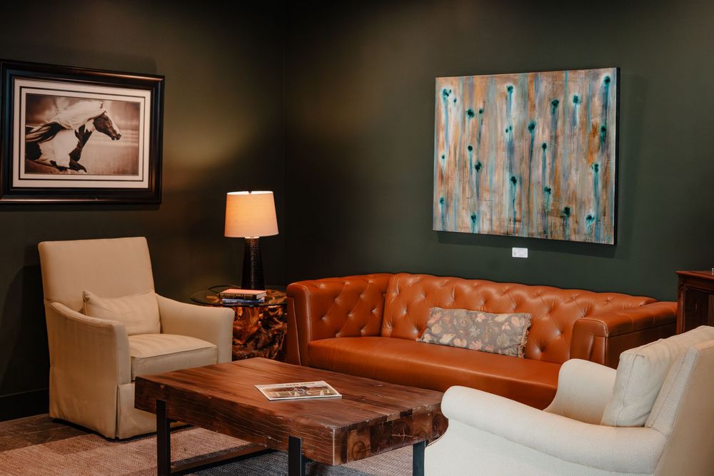 Elegant living room with orange leather tufted sofa, cream armchairs, wood coffee table, and modern art on dark walls.