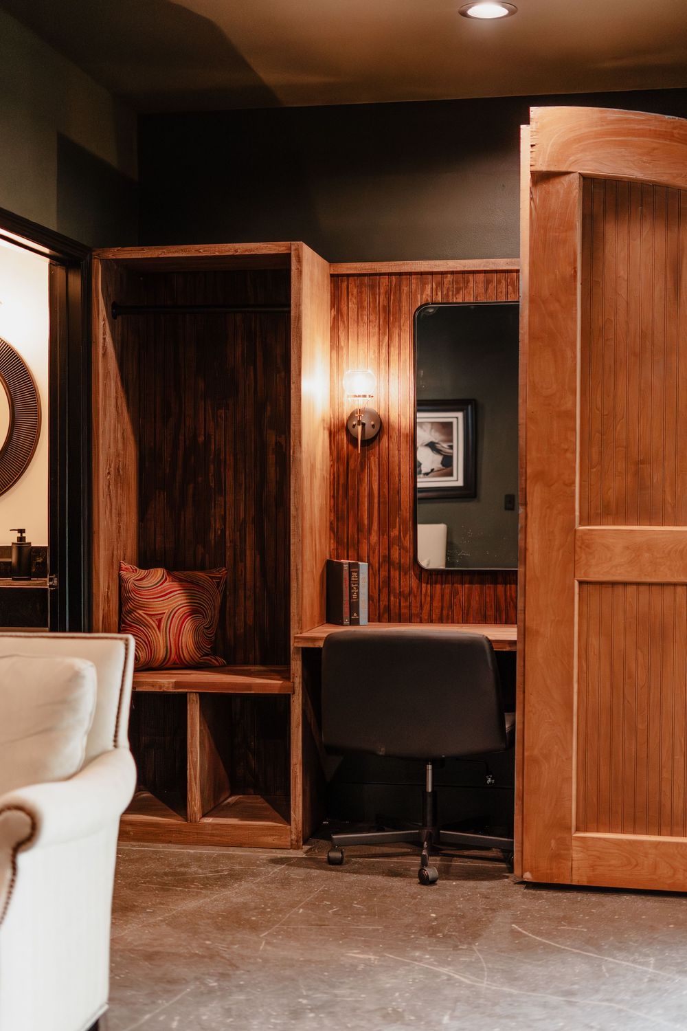 Elegant hotel suite workspace with rich wood built-in desk, cabinetry, and mirror with warm wall sconce lighting.