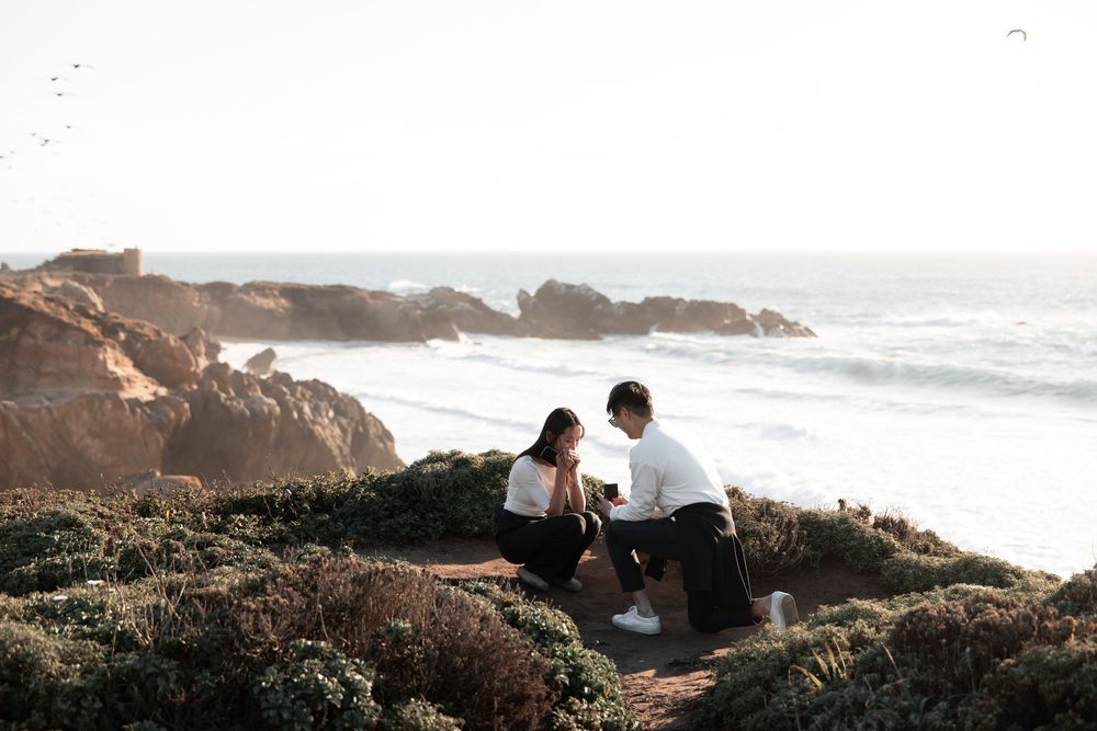 Couple sharing a romantic moment on rocky coastal cliffs with ocean waves in the background.