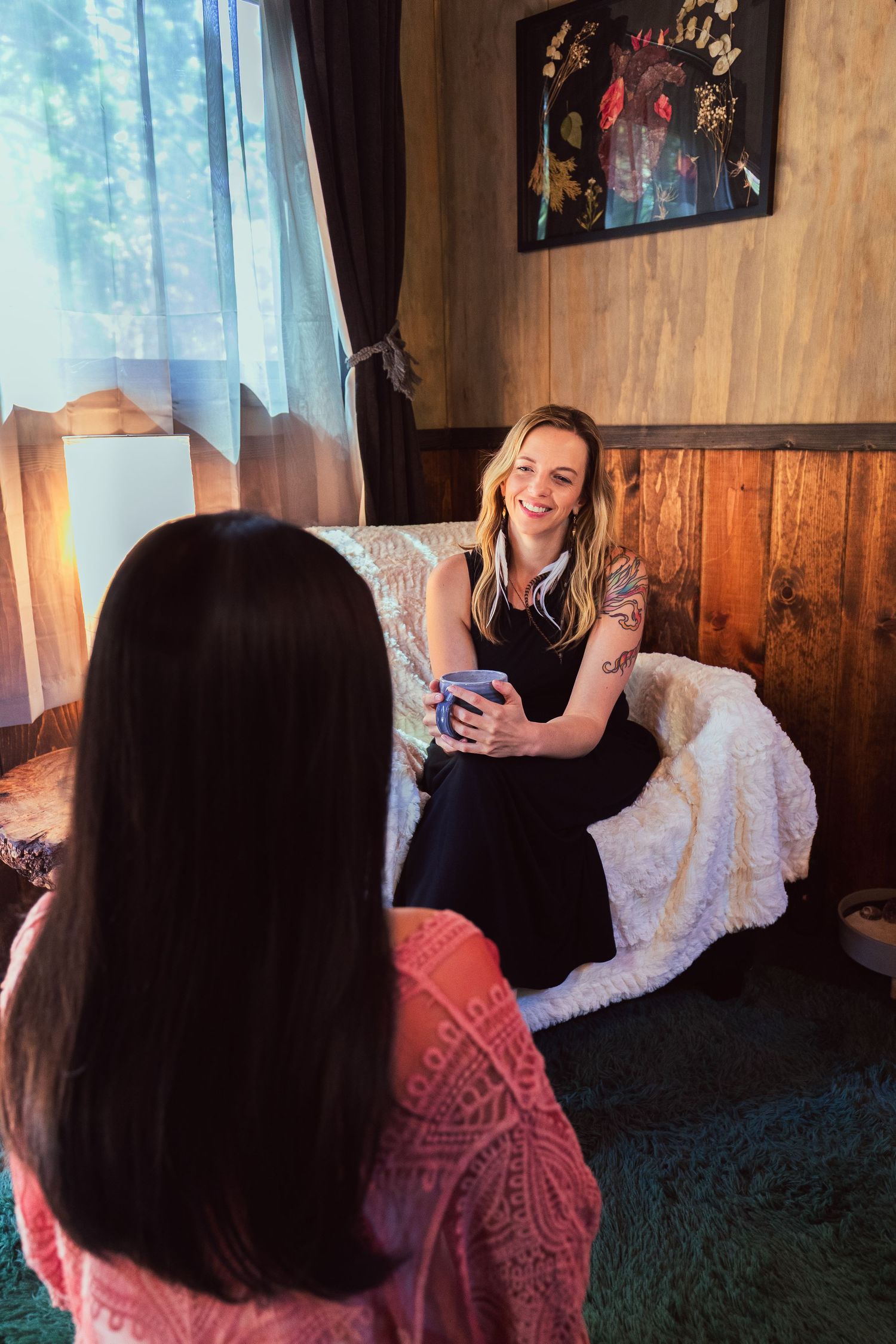 Two women enjoying conversation over coffee in a cozy wood-paneled living room with natural light.