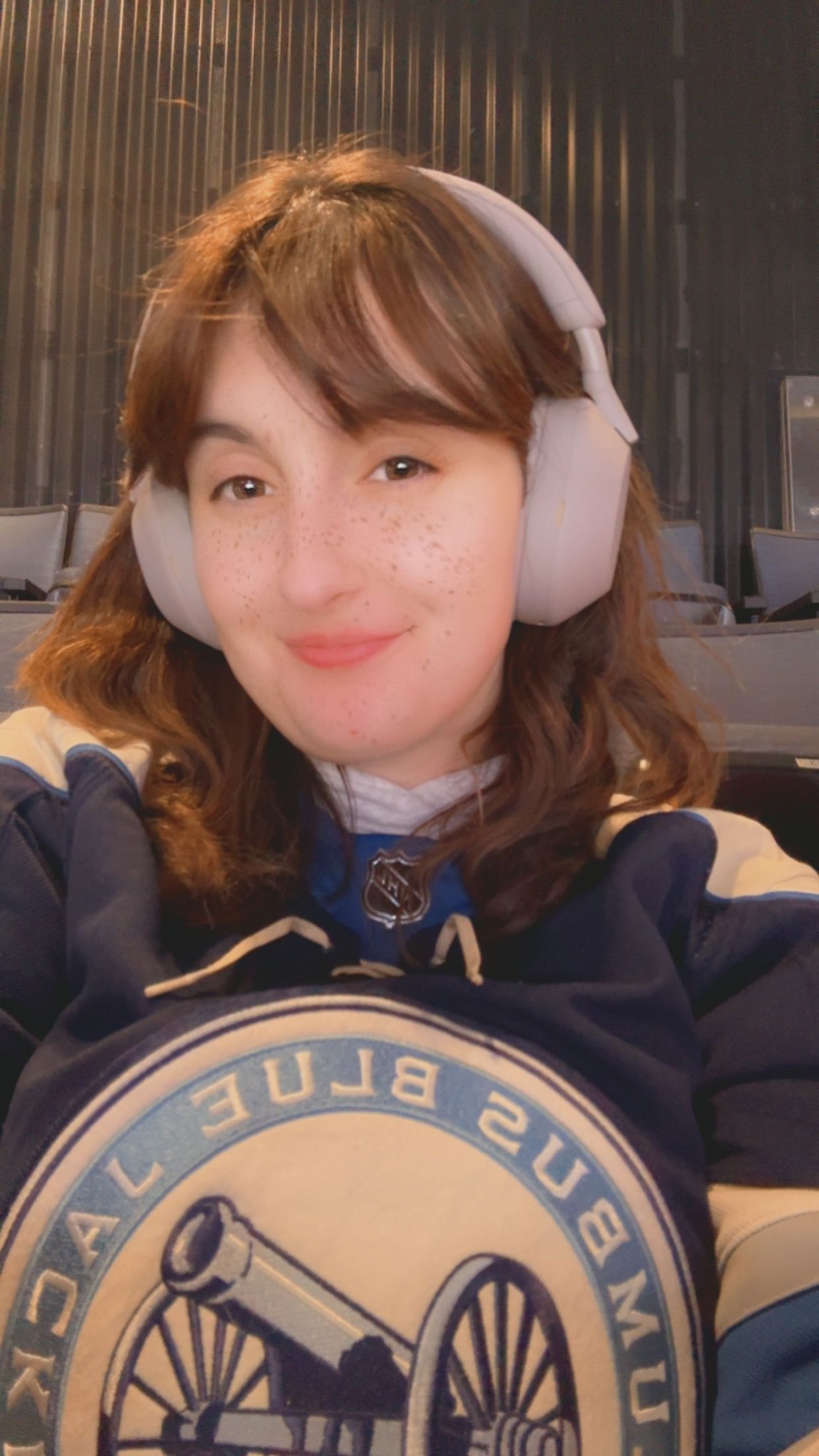 Person wearing white headphones and a Columbus Blue Jackets NHL hockey team sweatshirt smiles at camera.