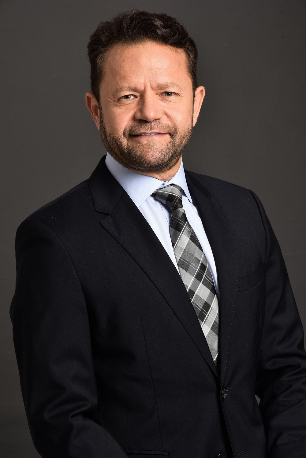 Professional headshot series against dark background wearing black suit and patterned tie.