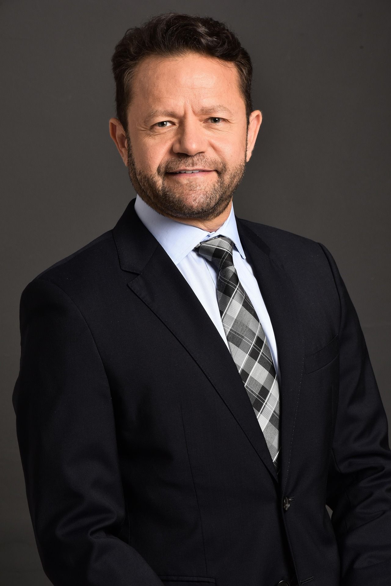 Professional headshot series against dark background wearing black suit and patterned tie.