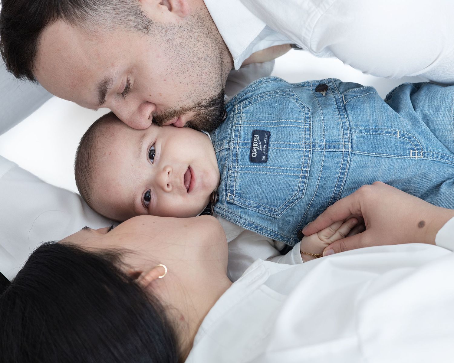A family sharing a tender moment together while lying on white bedding.