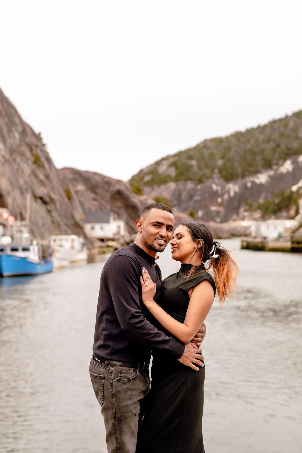 couple dressed in black kissing with Quidi Vidi harbour in the background, engagement session St. John's Newfoundland