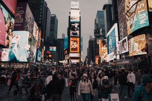 Crowded Times Square NYC at dusk with illuminated billboards and large pedestrian crowd.