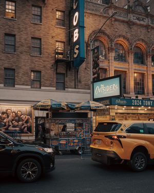 Broadway theater district street scene with yellow taxi and The Outsiders marquee sign.